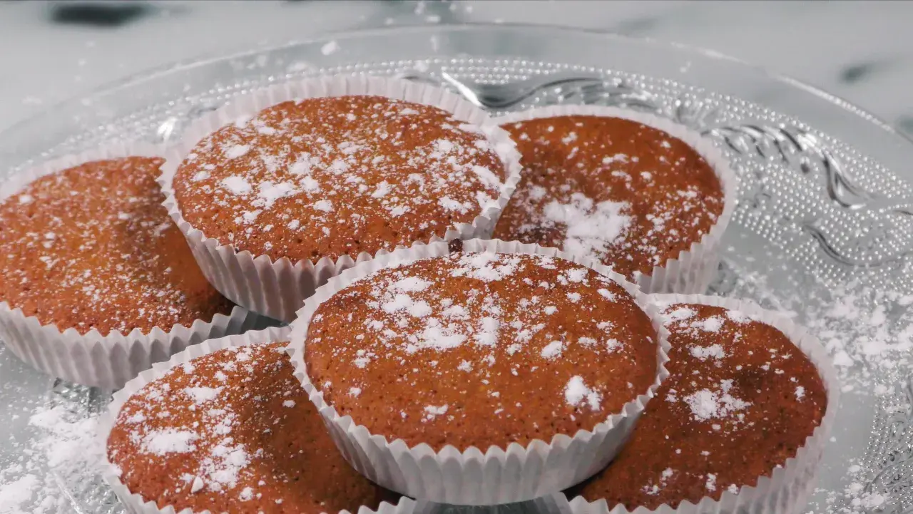 En hög med glutenfria saffransmuffins, pudrade med florsocker, ligger på ett vackert glasfat. Perfekt för fikat!