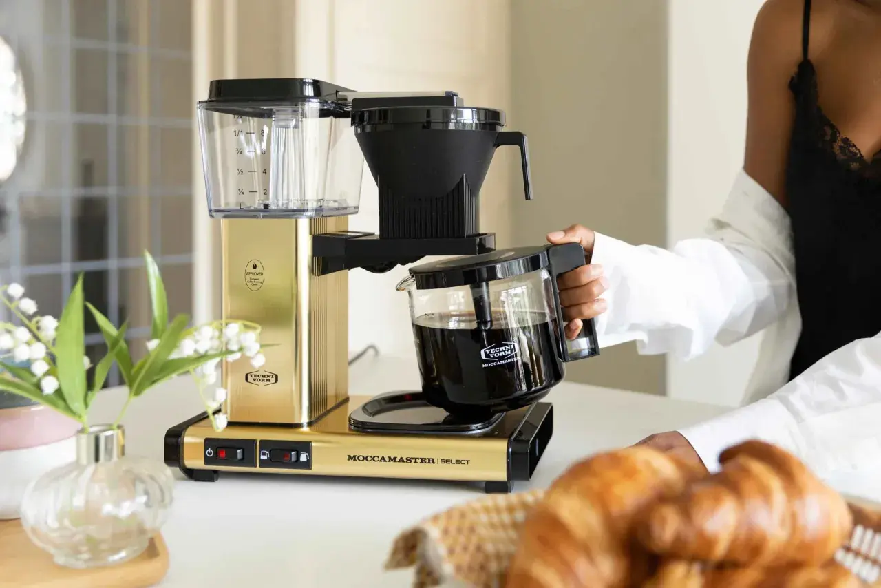 En guldfärgad Moccamaster kaffebryggare med en glaskanna fylld med kaffe. Denna modell är känd för sin optimala bryggtemperatur.