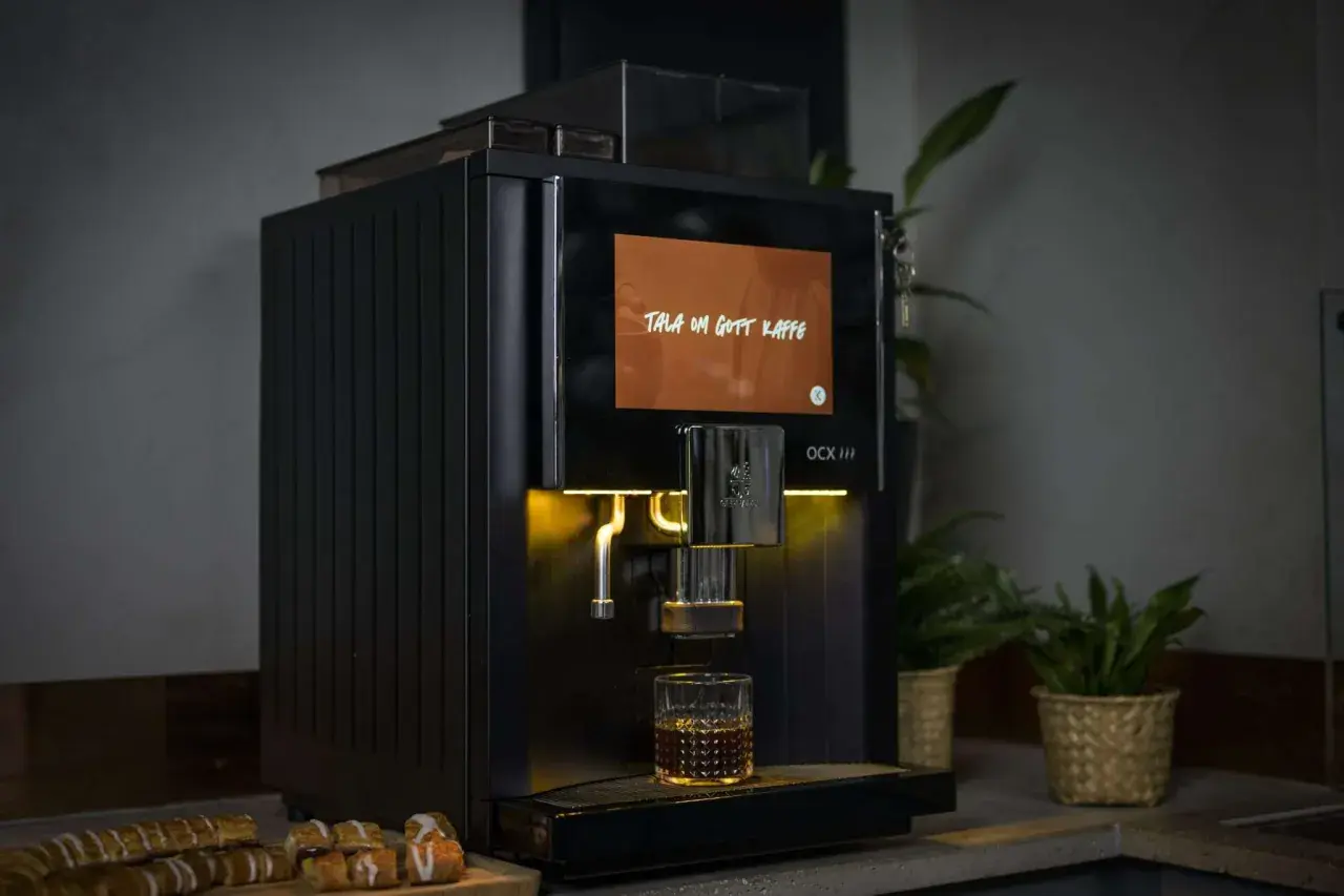 Svart kaffemaskin brygger en kopp kaffe, med texten "Tala om gott kaffe" på skärmen. Perfekt för dig som vill ha exakt rätt mängd gram kaffe per kopp.