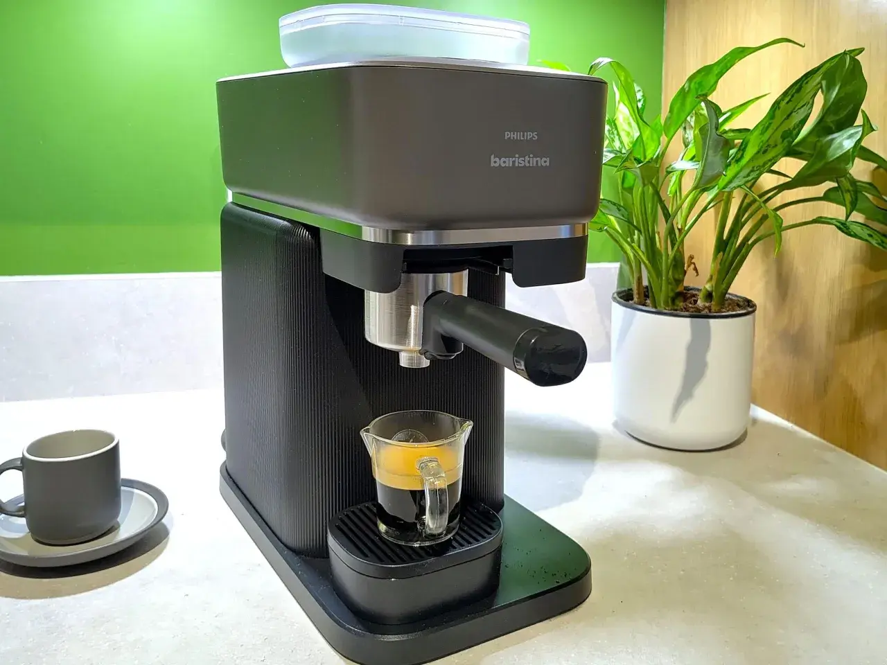 En Philips Baristina espressomaskin brygger en perfekt shot kaffe till espressomaskin. En grön vägg och en krukväxt i bakgrunden.