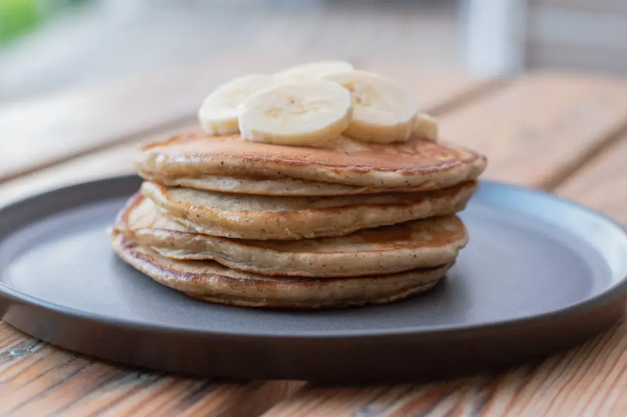 En hög med fluffiga bananpannkakor, toppad med bananskivor. Ett enkelt och gott bananpannkaka recept för frukost eller mellanmål.
