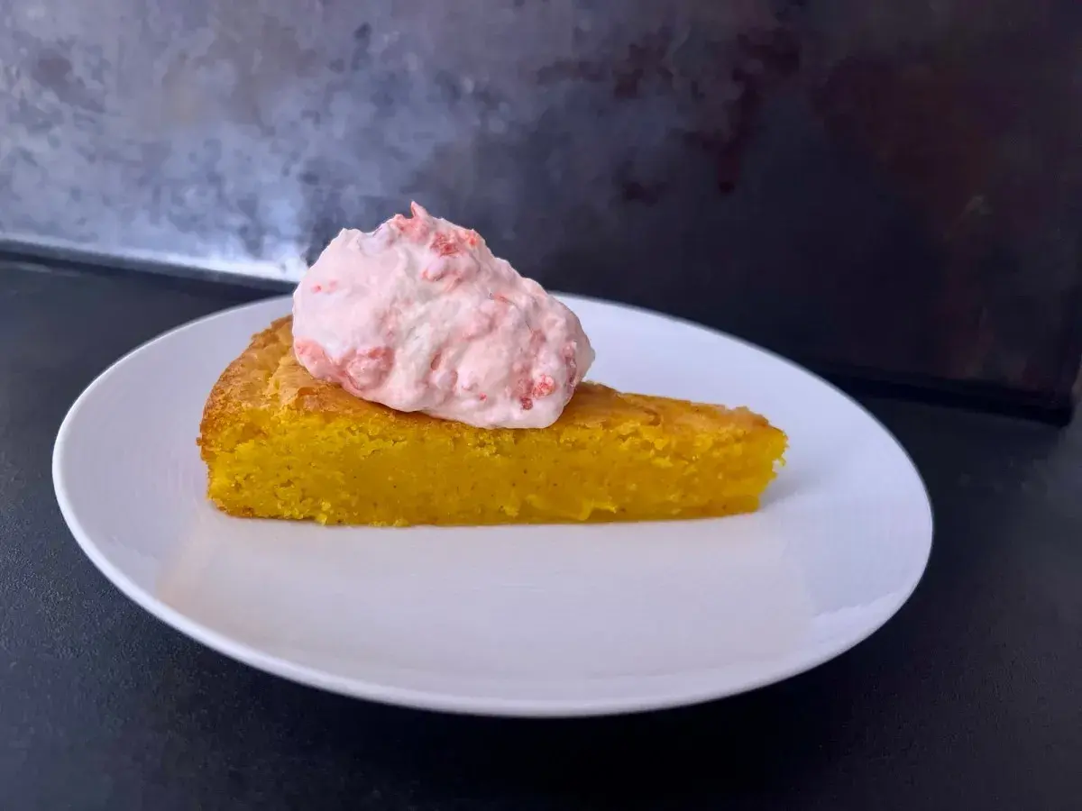 En bit glutenfri saffranskladdkaka med vit choklad, toppad med rosa grädde.