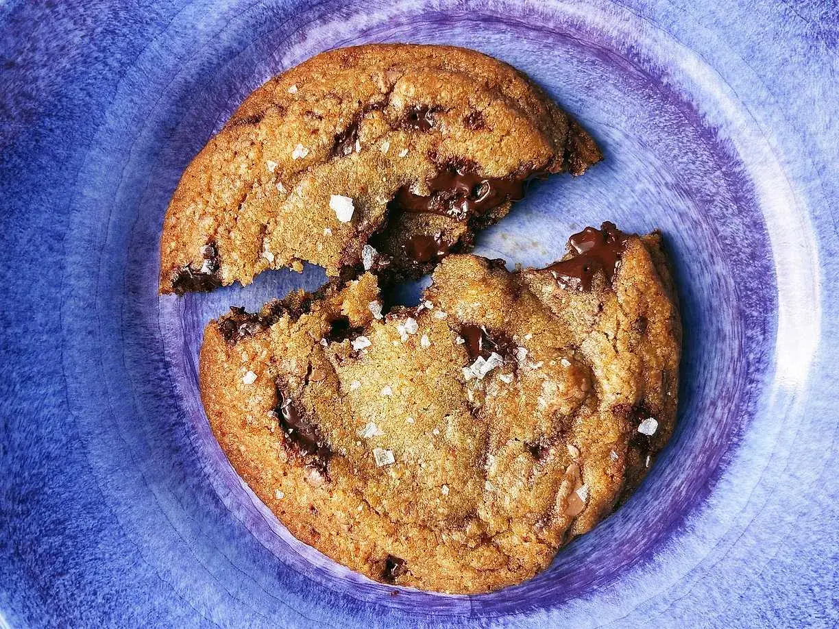 En chokladchipkaka, delad, med smält choklad som rinner ut. Strössel av flingsalt.