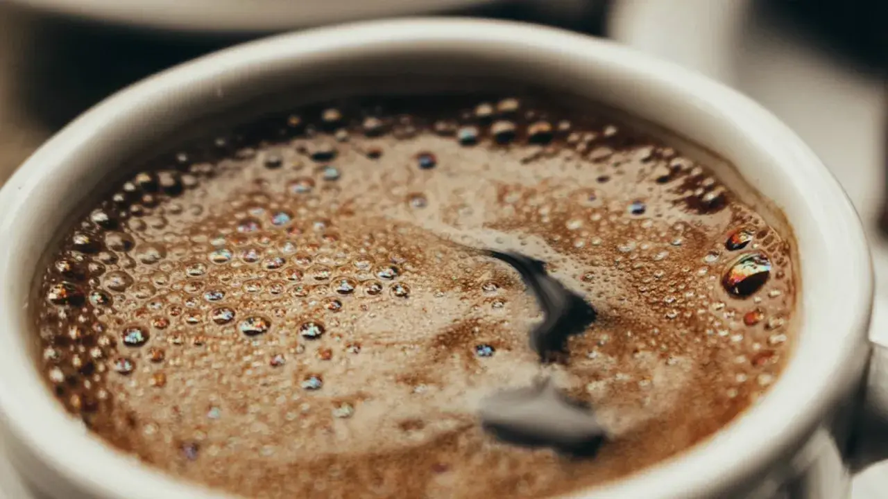 En vit kopp med bubbligt java kaffe. Skummet har regnbågsskimrande bubblor och en mörk virvel i mitten.
