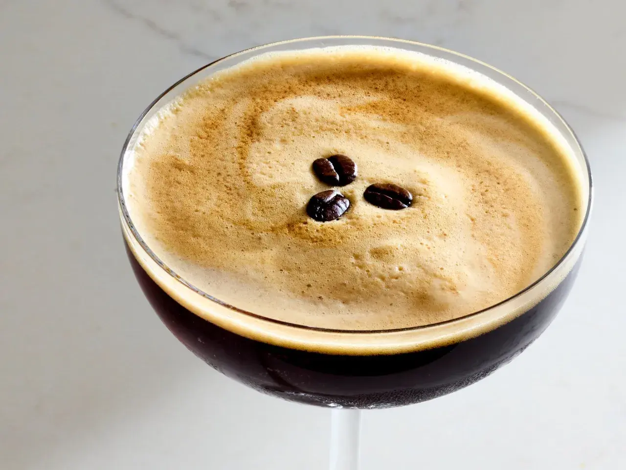 En perfekt espresso martini med krämigt skum och tre kaffebönor som dekoration.