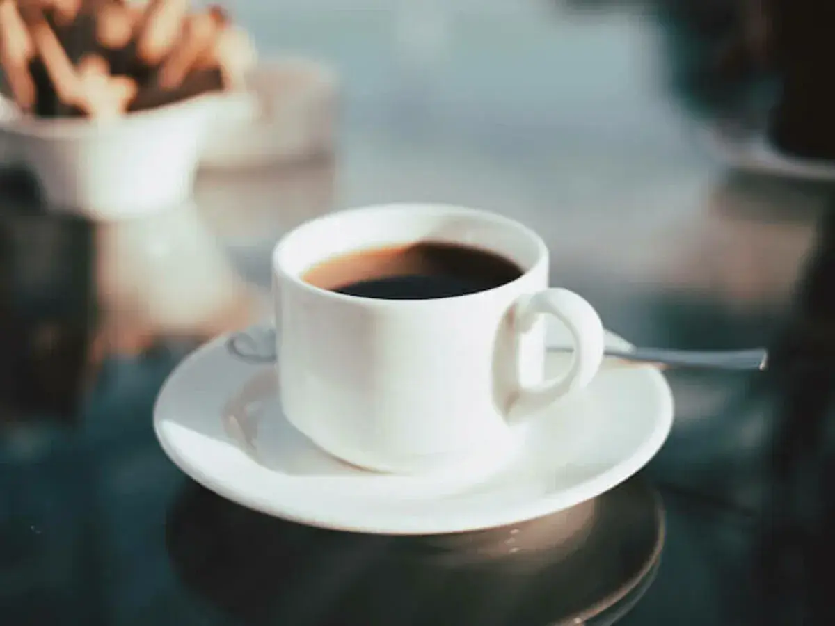 En kopp med **temp rostas** kaffe står på ett fat. I bakgrunden syns en skål med kex.