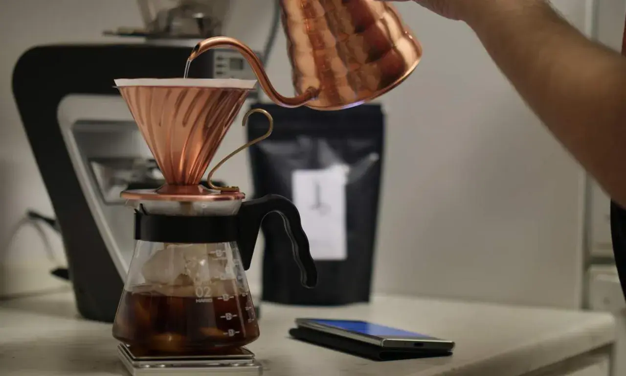 En person häller varmt vatten över kaffepulver i en kopparfilterhållare för att brygga kaffe manuellt.