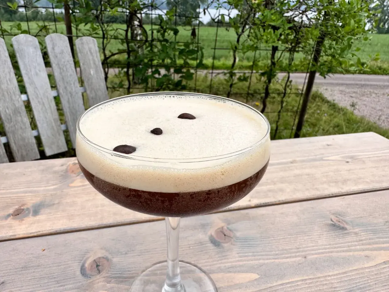 En härlig espresso martini med krämigt skum och tre kaffebönor, perfekt för en stunds avkoppling utomhus.