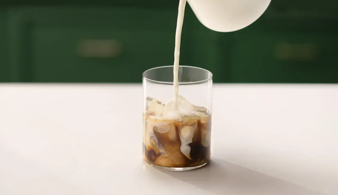 Mjölk hälls i ett glas med is och kaffe. Ett perfekt iskaffe recept för en varm dag.