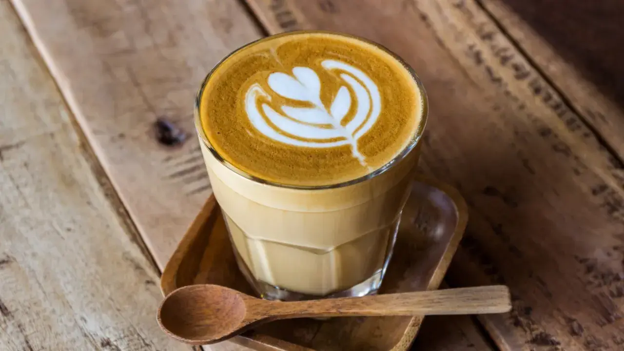 En vacker latte med mjölkskum som bildar ett mönster, serverad med en träsked. Perfekt kaffe för en mysig stund.