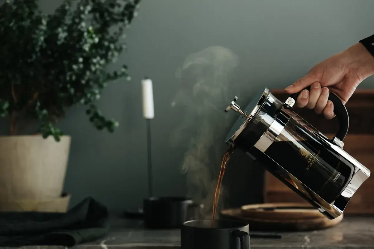 En hand häller upp ångande kaffe ur en presskanna. Perfekt presskaffe tid.