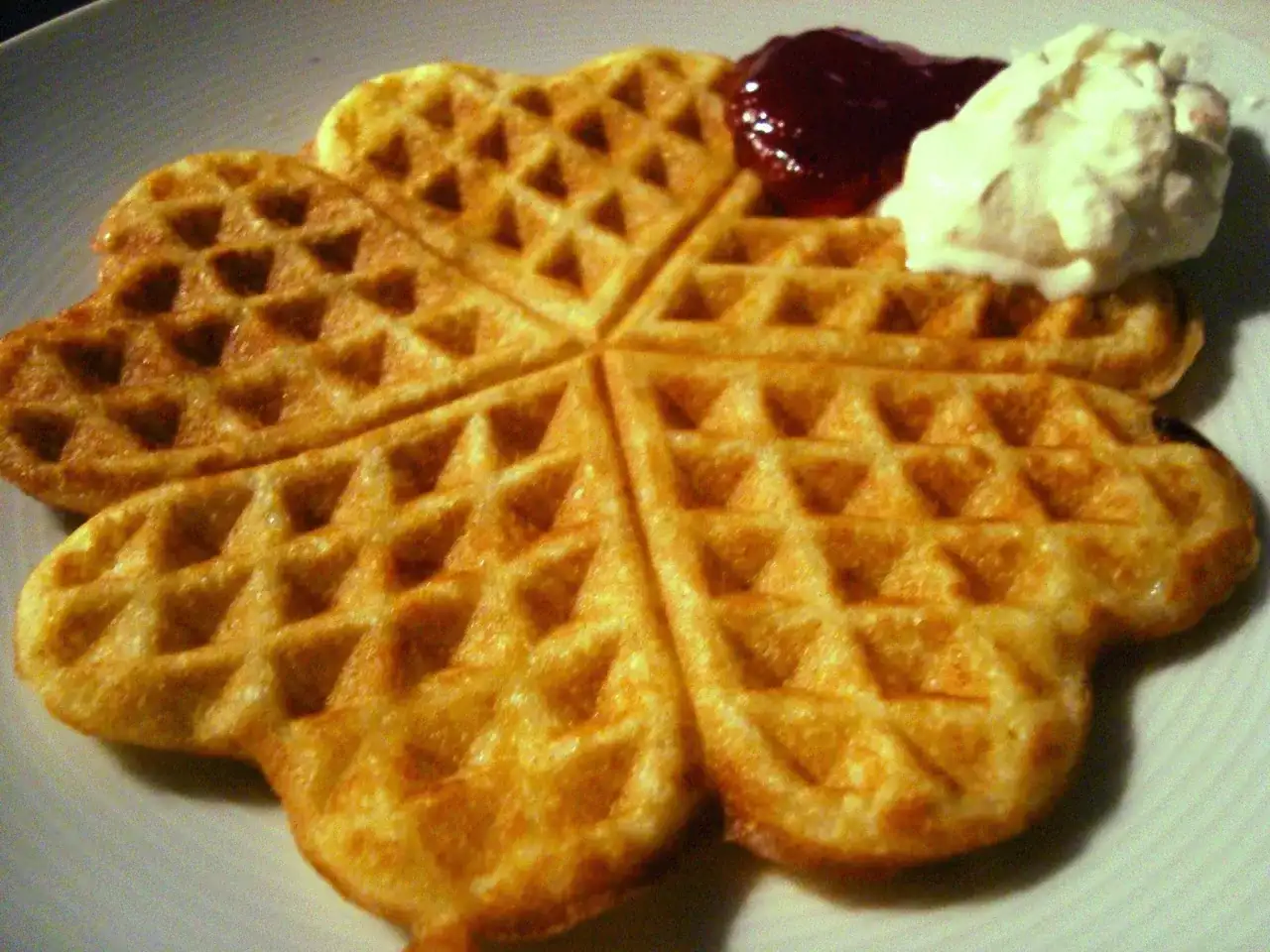 Golden-brown heart-shaped waffles with jam and whipped cream.
