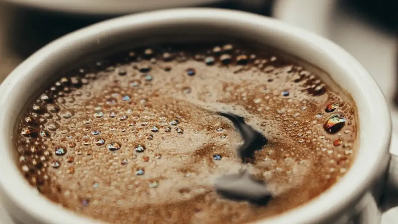 En vit kopp med bubbligt java kaffe. Skummet har regnbågsskimrande bubblor och en mörk virvel i mitten.