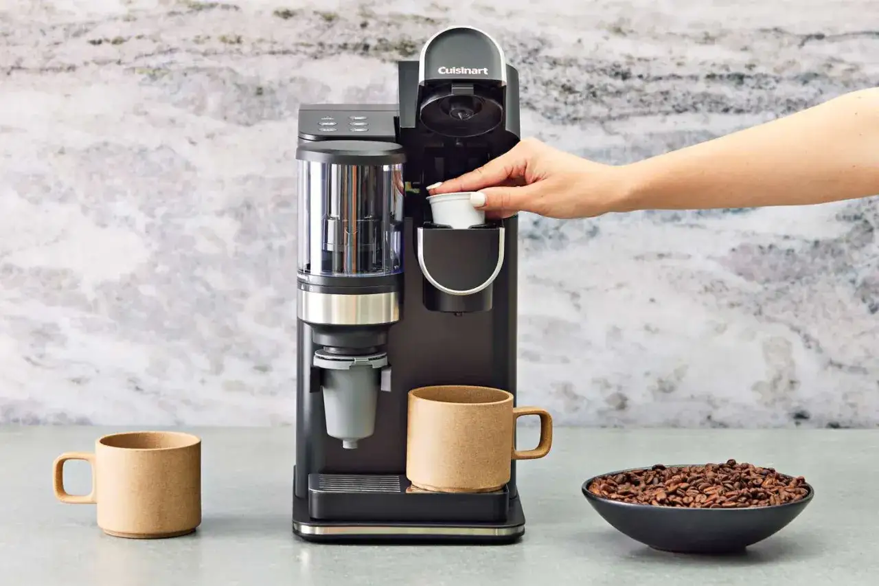 En hand placerar en kaffekapsel i en Cuisinart-maskin. Bredvid står en mugg och en skål med bönor. Undrar du hur mycket koffein i en kopp kaffe?