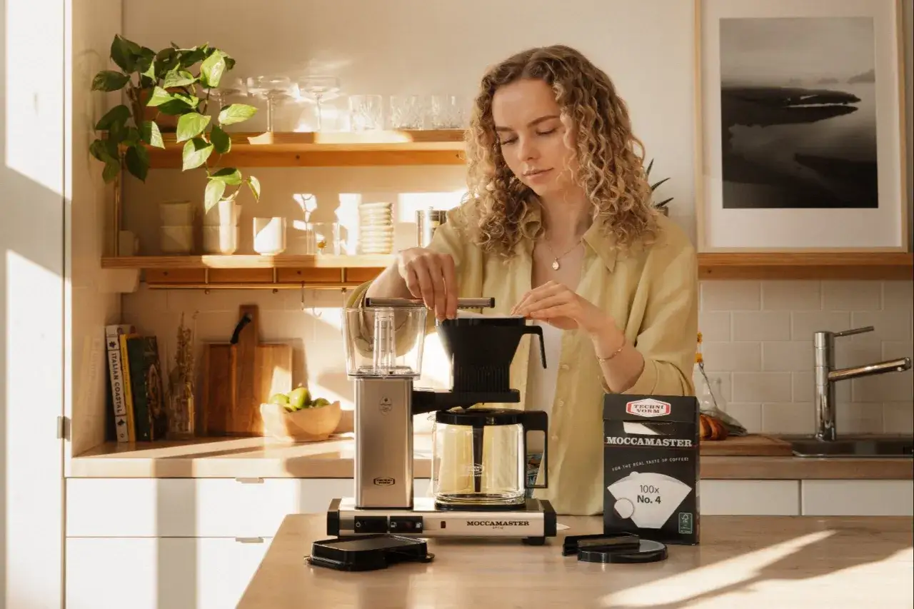 En kvinna förbereder kaffe med en Moccamaster. Hon funderar på hur många skopor kaffe till 2 koppar.