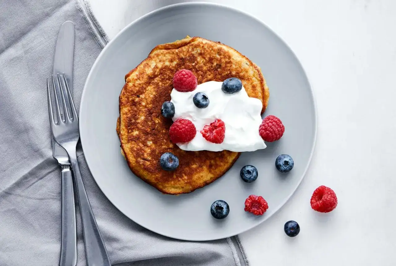 En gyllene bananpannkaka toppad med grädde och bär. Ett perfekt bananpannkaka recept för en härlig frukost.