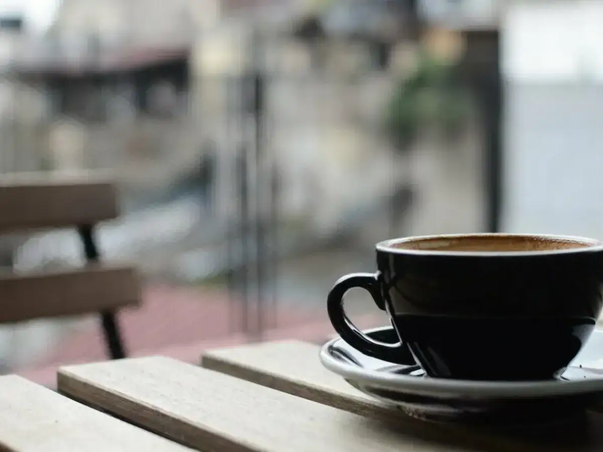 En svart kopp med lungo kaffe st&aring;r p&aring; ett tr&auml;bord. I bakgrunden syns en b&auml;nk och en suddig stadsmilj&ouml;.