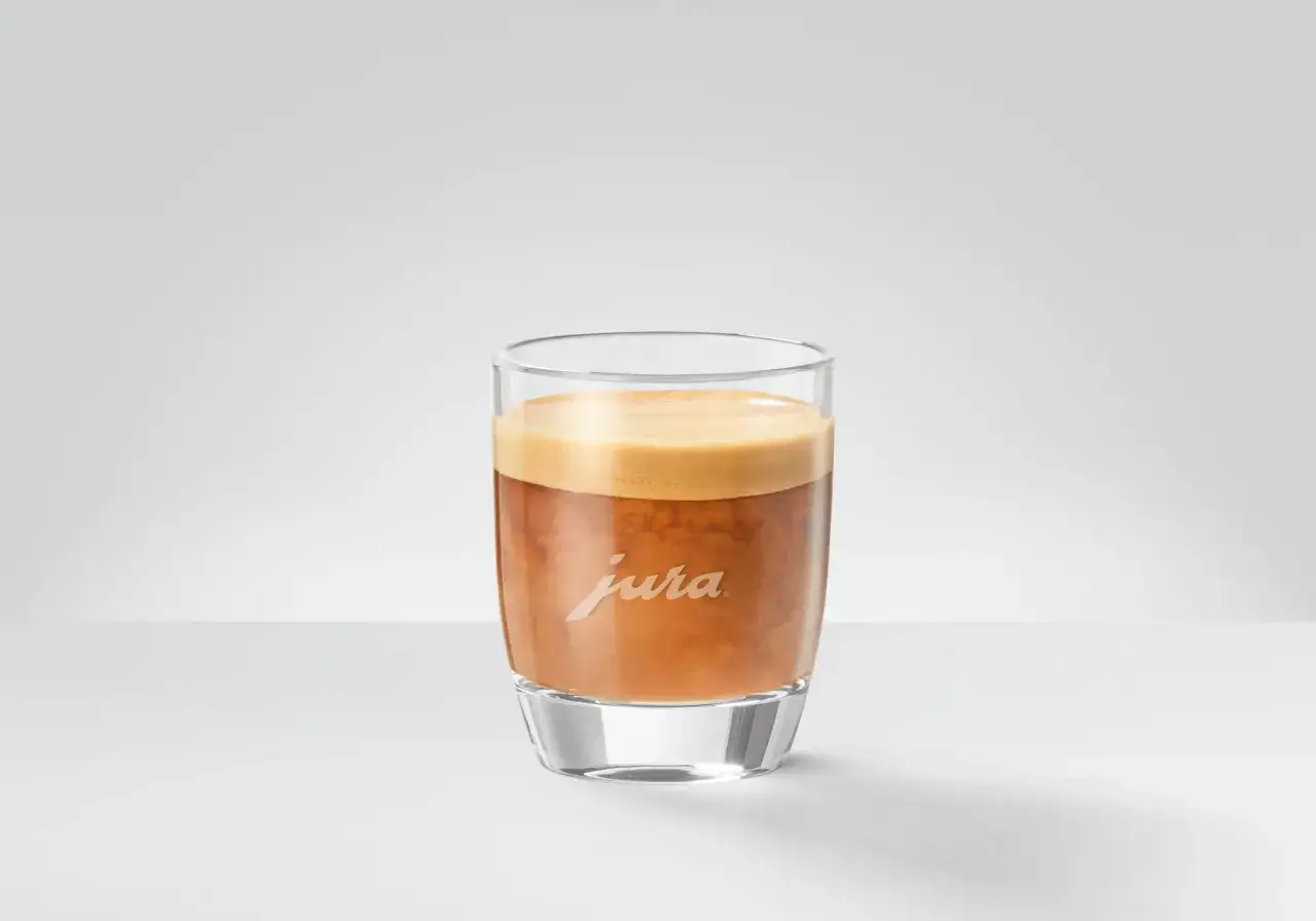 En perfekt cafe cortado i ett glas med Jura-logotyp.