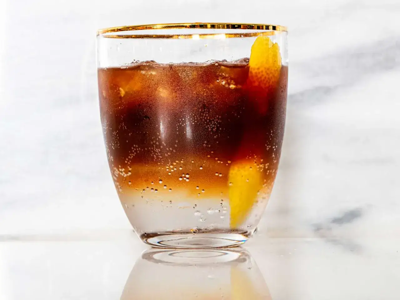 Ett glas med kaffe tonic, is och en citronskal. Bubblorna dansar i den mörka drycken.