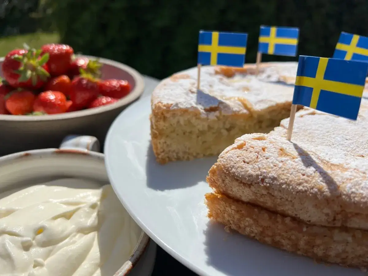 En härlig glutenfri sverigekaka med svenska flaggor, serverad med jordgubbar och grädde. Perfekt för nationaldagen!