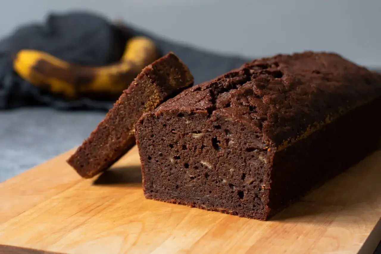 En saftig banankaka med choklad, en skiva uppskuren, med en övermogen banan i bakgrunden.