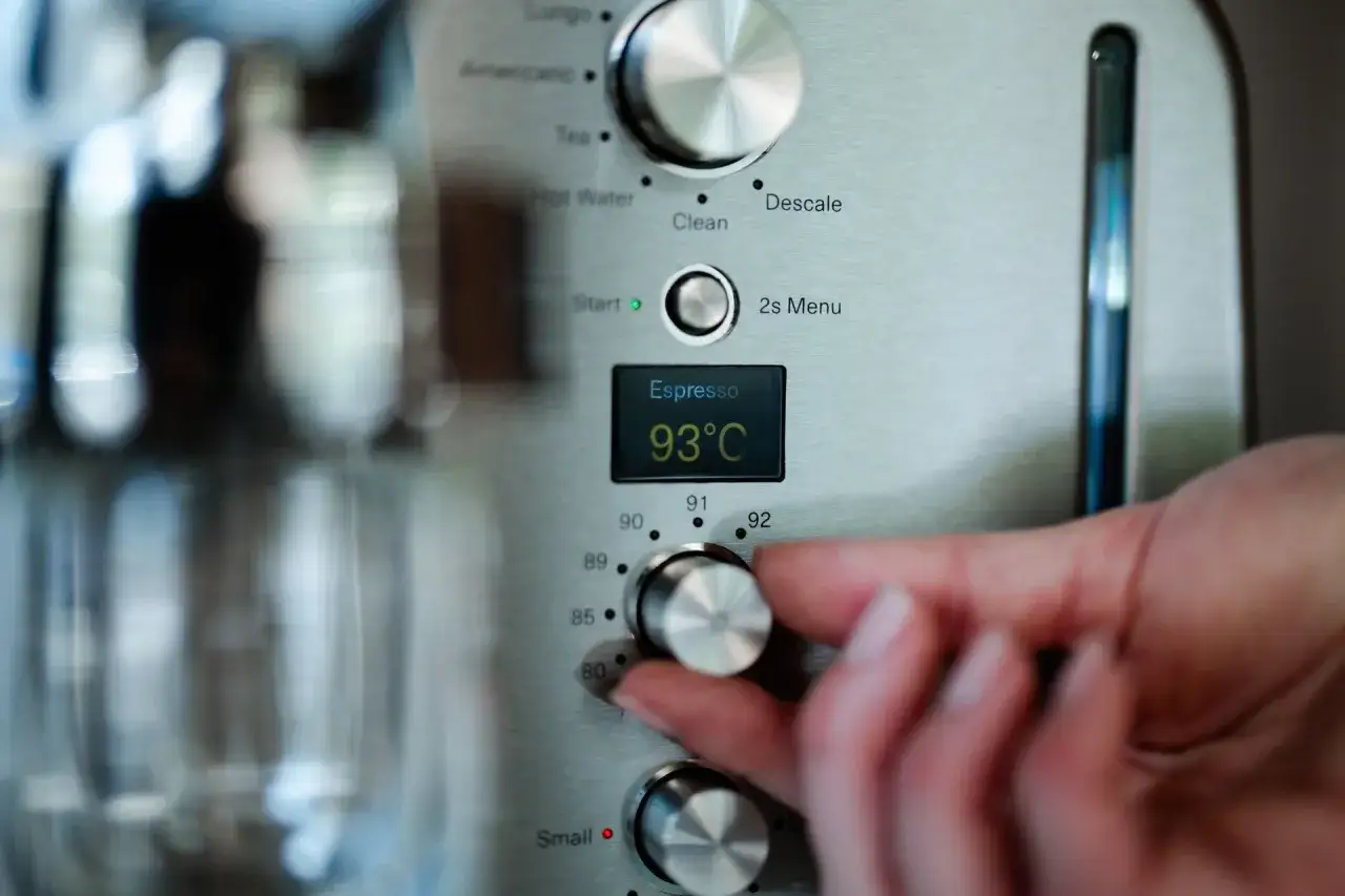 En hand justerar vredet på en espressomaskin för att ställa in kaffe temperatur till 93°C.