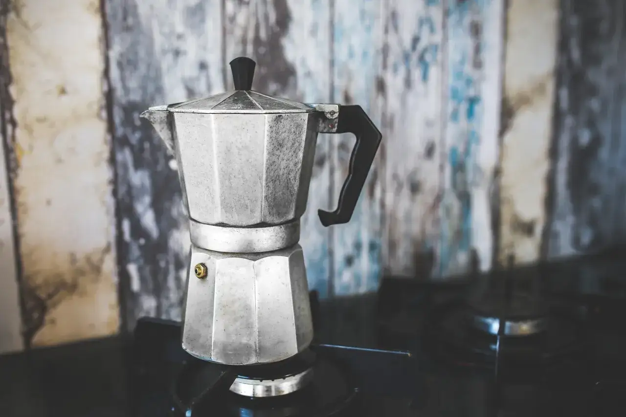 En klassisk perkulator st&aring;r p&aring; spisen, redo att koka kaffe. Bakgrunden &auml;r en sliten tr&auml;v&auml;gg.