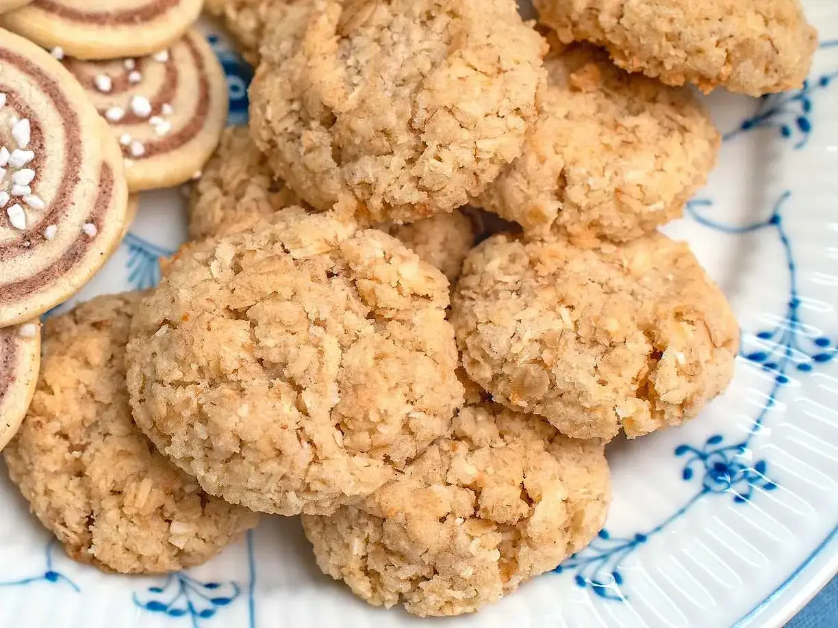 En h&ouml;g med hembakade havrekakor med kokos, med en textur som inbjuder till fika. Bredvid syns n&aring;gra rullade kakor med p&auml;rlsocker.