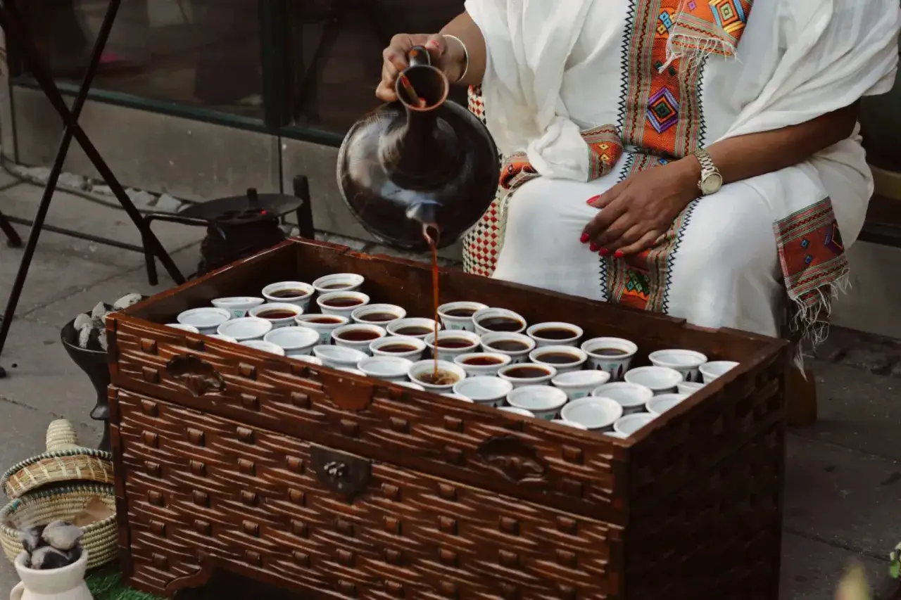 En kvinna h&auml;ller upp kaffe ur en traditionell jebena i sm&aring; koppar. En vacker scen som ber&auml;ttar om kaffe historia.