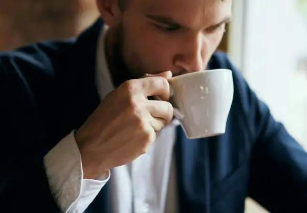 En man i kostym tar en klunk kaffe ur en vit kopp. Kanske blir man pigg av kaffe.