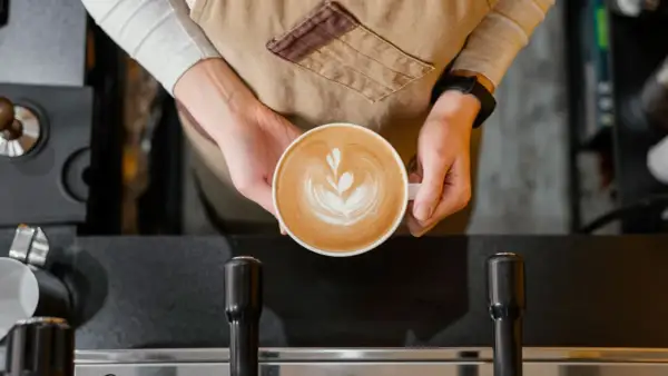 Barista håller en vacker latte med latte art. Undrar hur många koppar kaffe per paket Zoegas det blir?