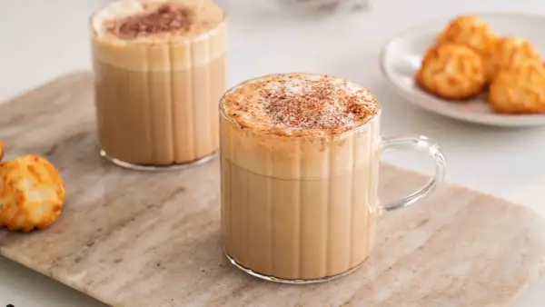 Två glas med krämiga kaffedrinkar, toppade med kanel och en liten tallrik med makroner. Perfekt för inspiration till egna kaffedrinkar recept.