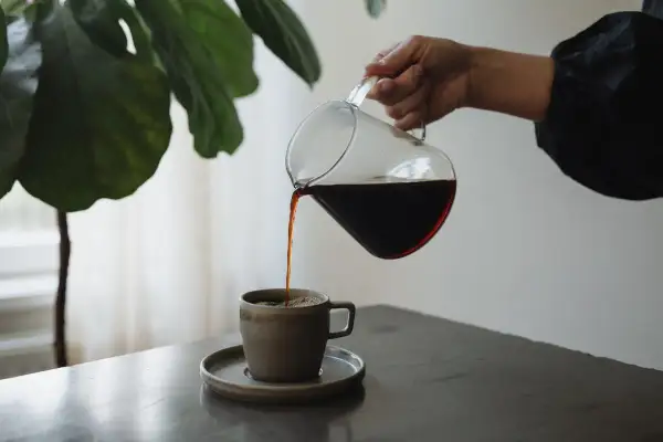 En hand häller upp mörkt kaffe från en glaskanna i en mugg. En fin stund för att njuta av kaffe, inte espresso.