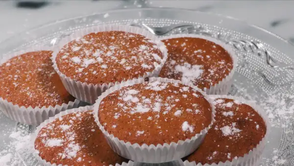 En hög med glutenfria saffransmuffins, pudrade med florsocker, ligger på ett vackert glasfat. Perfekt för fikat!