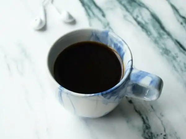 En kopp kaffe, perfekt för att njuta av ditt americano recept. Vita hörlurar ligger bredvid.