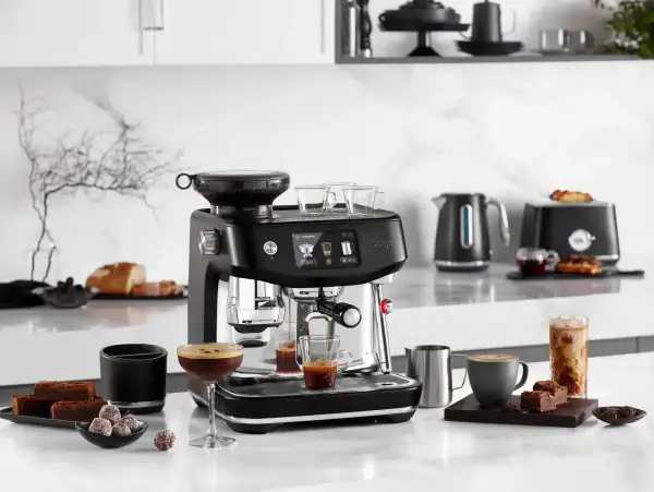 Svart espressomaskin med kaffekoppar, chokladbitar och en glasburk med iskaffe. Perfekt för att brygga gott kaffe oavsett om du har hårt eller mjukt vatten.