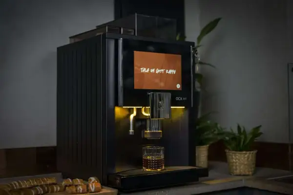 Svart kaffemaskin brygger en kopp kaffe, med texten "Tala om gott kaffe" på skärmen. Perfekt för dig som vill ha exakt rätt mängd gram kaffe per kopp.
