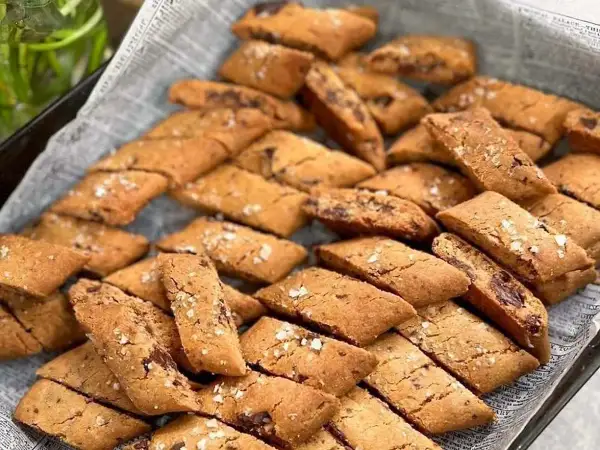 En hög med hembakade kolakakor med chokladbitar, strösslade med flingsalt. Perfekt för ett kolakakor recept!