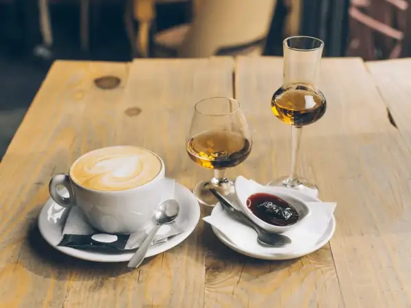 En kopp cappuccino med hjärtkonst, två glas avec och en skål med sylt. Perfekt avec till kaffet.