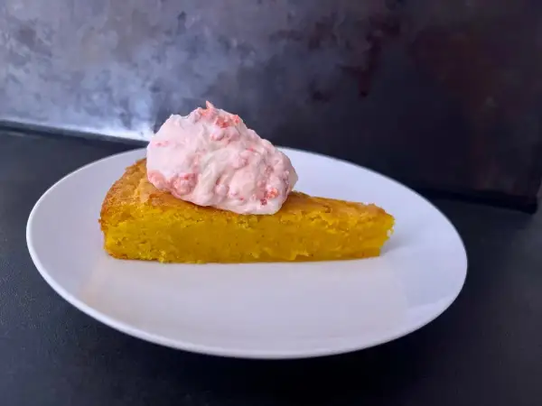 En bit glutenfri saffranskladdkaka med vit choklad, toppad med rosa grädde.
