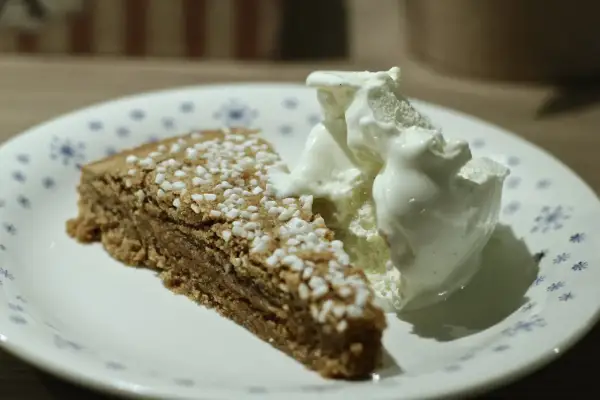 En bit glutenfri kanelbullekladdkaka med en kula vaniljglass på en tallrik med blå blommor.