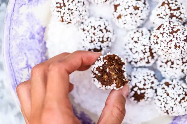 En hand håller en bit av lyxiga chokladbollar, rullade i vita pärlsocker.