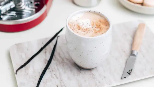En krämig vaniljlatte hemma, med vaniljstänger och en liten kniv på en marmorerad bricka.