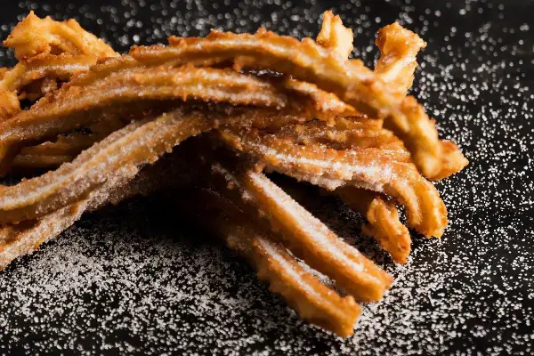 Krispiga churros, pudrade med socker, redo att avnjutas. Ett perfekt churros recept för hemmabruk.