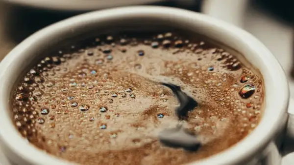 En vit kopp med bubbligt java kaffe. Skummet har regnbågsskimrande bubblor och en mörk virvel i mitten.