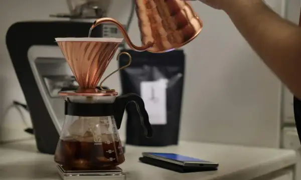 En person häller varmt vatten över kaffepulver i en kopparfilterhållare för att brygga kaffe manuellt.