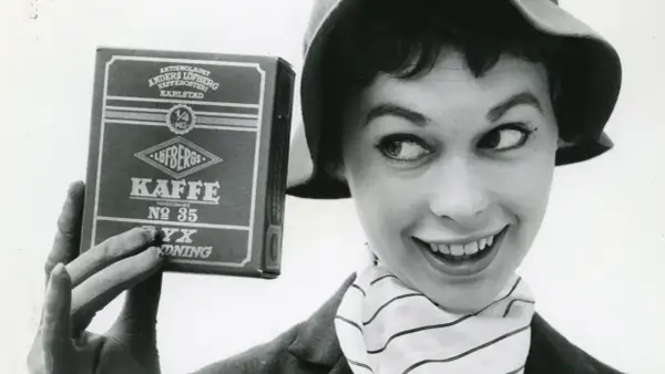 En kvinna med hatt och randig scarf håller upp en låda Löfbergs Kaffe. Kanske hon vet vilka som dricker mest kaffe i Sverige?