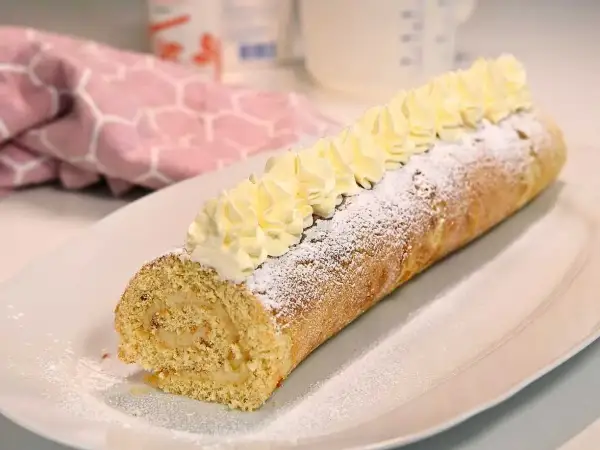 En härlig semmelrulltårta glutenfri, pudrad med florsocker och toppad med grädde. Perfekt för fikat!