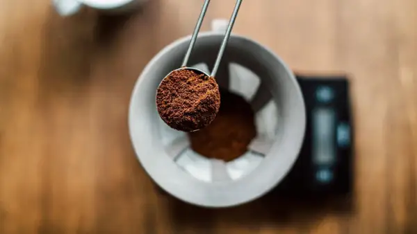Malen kaffepulver hälls från en skopa ner i en filterhållare, redo för bryggning. Rätt kaffe temperatur är avgörande för smaken.