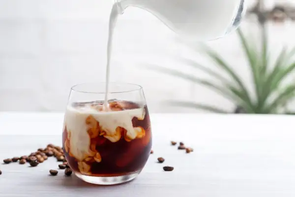 Mjölk hälls i ett glas med iskaffe och kaffebönor, en perfekt islatte.